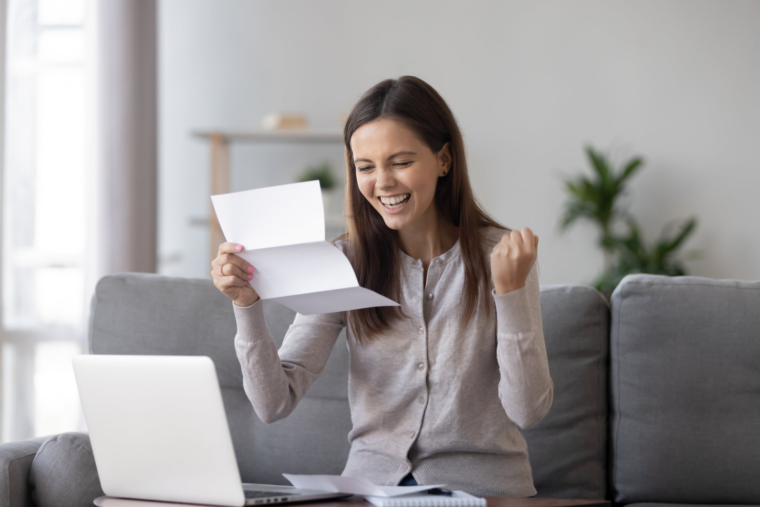 woman sitting on couch and looking excited while reading a letter